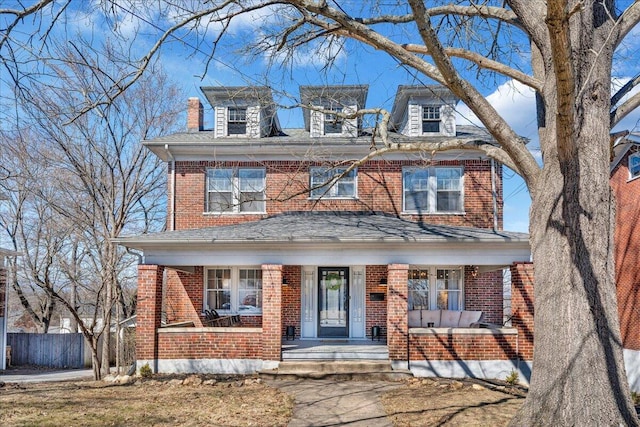 traditional style home featuring brick siding, covered porch, roof with shingles, and fence