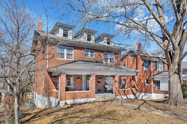 american foursquare style home featuring brick siding, a porch, and a chimney