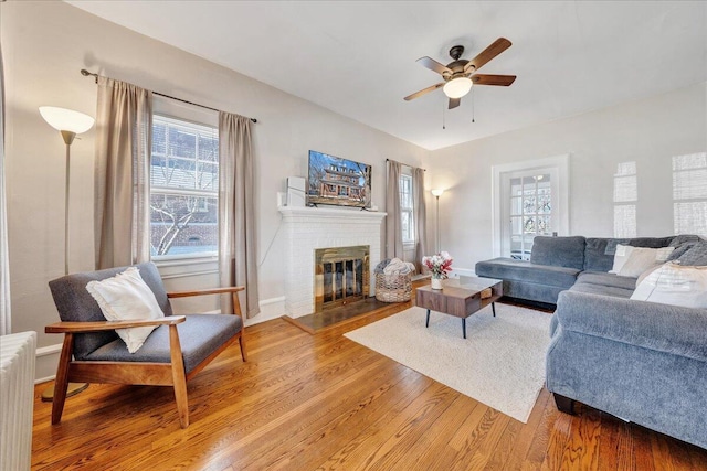 living area featuring light wood-type flooring, radiator, a fireplace, baseboards, and ceiling fan