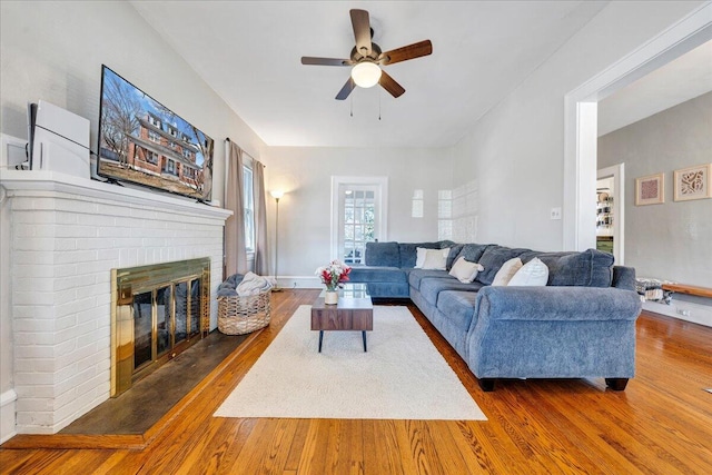 living area with a brick fireplace, baseboards, a ceiling fan, and wood finished floors