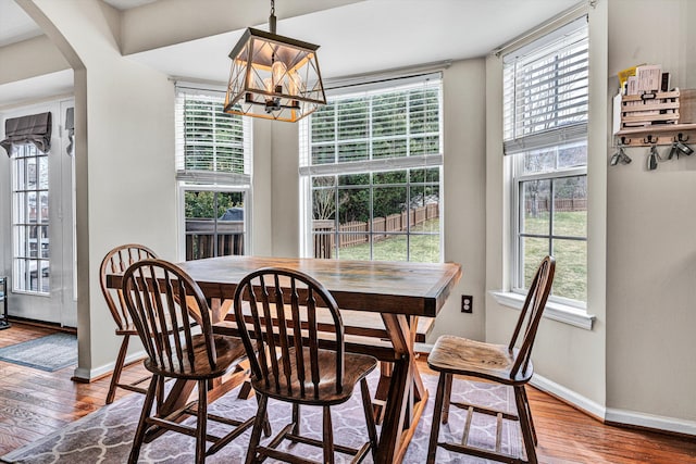 dining space featuring wood-type flooring, arched walkways, a chandelier, and plenty of natural light