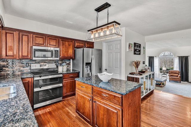 kitchen featuring tasteful backsplash, open floor plan, hardwood / wood-style floors, dark stone counters, and appliances with stainless steel finishes