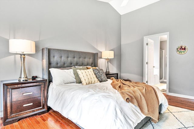 bedroom featuring baseboards, lofted ceiling, ensuite bath, and wood finished floors