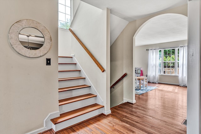 staircase with arched walkways, visible vents, baseboards, and wood finished floors