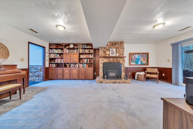 living area featuring a wood stove, light carpet, visible vents, and wainscoting