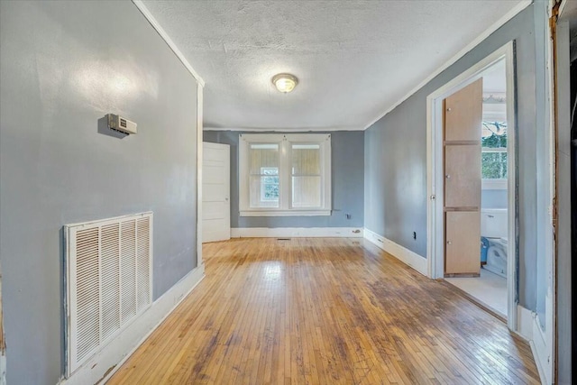 unfurnished room with hardwood / wood-style flooring, a textured ceiling, baseboards, visible vents, and ornamental molding