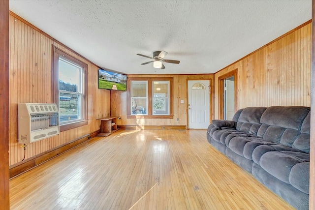 living area featuring heating unit, a ceiling fan, wood walls, a textured ceiling, and hardwood / wood-style floors