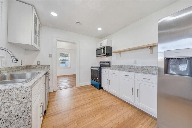 821 Kerns Ave SW, Roanoke, VA 24015 - kitchen with appliances with stainless steel finishes, open shelves, white cabinetry, light wood finished floors, and glass insert cabinets