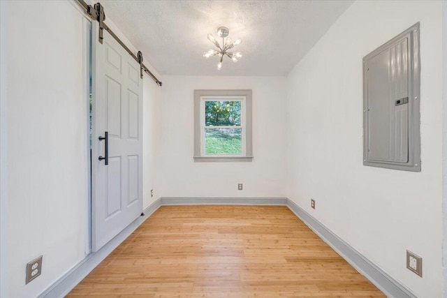 821 Kerns Ave SW, Roanoke, VA 24015 - unfurnished room with a barn door, electric panel, light wood-type flooring, a textured ceiling, and a chandelier