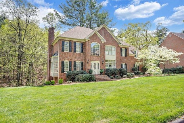 colonial house featuring a chimney, a front yard, and brick siding
