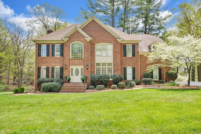 view of front of home with roof with shingles, brick siding, a front lawn, and a chimney