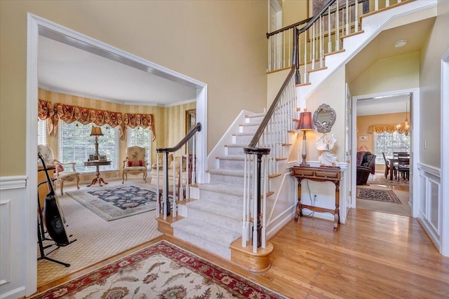 entrance foyer with wood finished floors, a decorative wall, wainscoting, a chandelier, and stairs