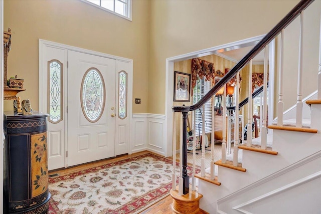 foyer entrance featuring stairway, wainscoting, a towering ceiling, and wood finished floors