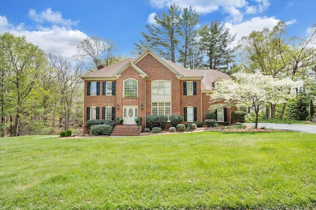 colonial home with a front lawn, brick siding, and a chimney