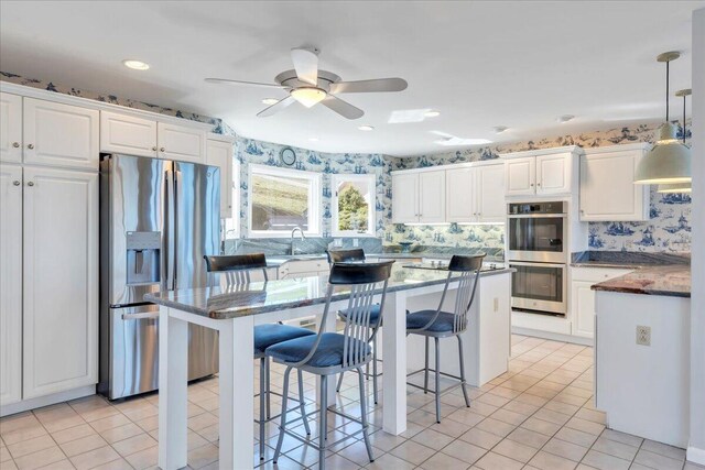 kitchen featuring a kitchen breakfast bar, light tile patterned floors, white cabinets, and stainless steel appliances