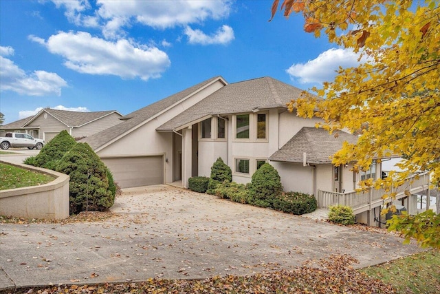 view of front facade with a shingled roof, concrete driveway, an attached garage, and stucco siding