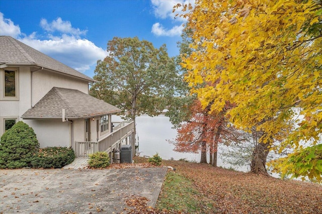 view of home's exterior with a shingled roof, cooling unit, a water view, and stucco siding