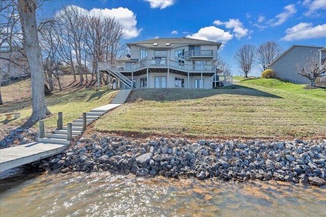 rear view of house with stairway, a lawn, and a deck with water view