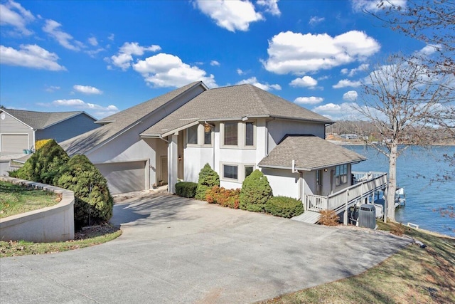 view of front facade featuring stucco siding, driveway, a garage, and a water view