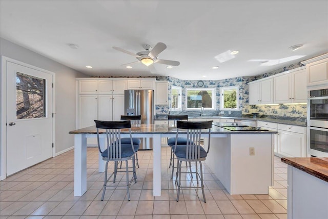 kitchen featuring light tile patterned flooring, stainless steel appliances, white cabinetry, dark countertops, and a kitchen breakfast bar