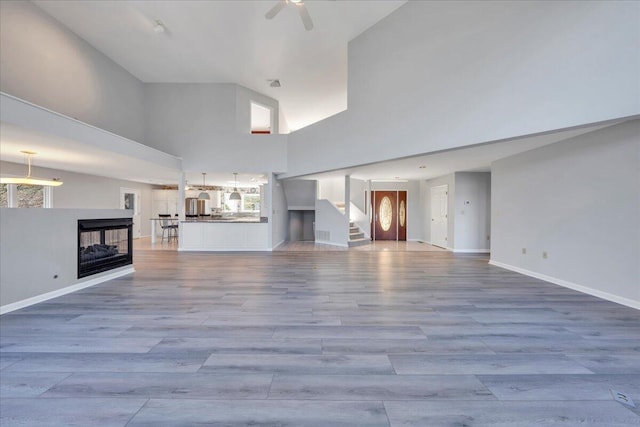 unfurnished living room featuring visible vents, baseboards, a towering ceiling, wood finished floors, and a ceiling fan