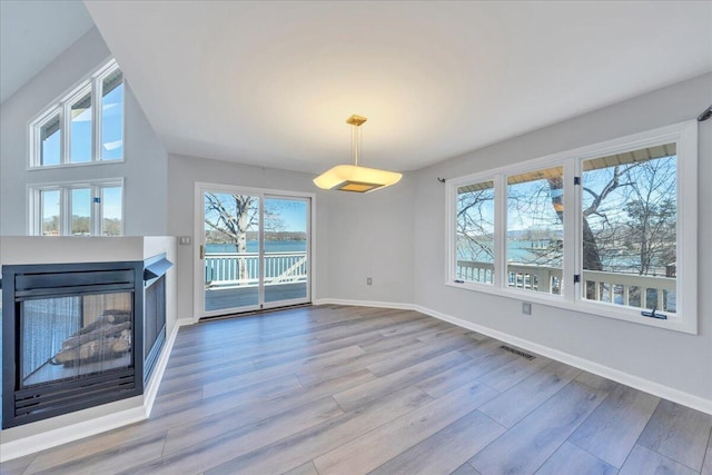unfurnished living room with a multi sided fireplace, visible vents, baseboards, and wood finished floors