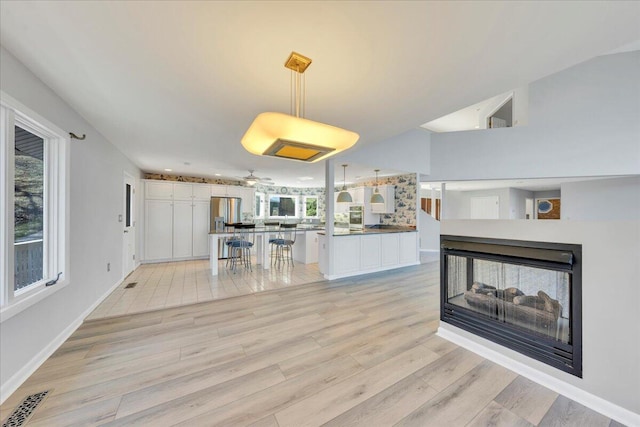 kitchen with visible vents, a multi sided fireplace, light wood-style flooring, freestanding refrigerator, and white cabinetry