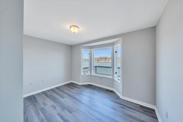 empty room featuring visible vents, a water view, baseboards, and wood finished floors