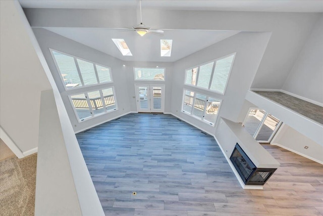 unfurnished living room with ceiling fan, wood finished floors, a skylight, and a fireplace