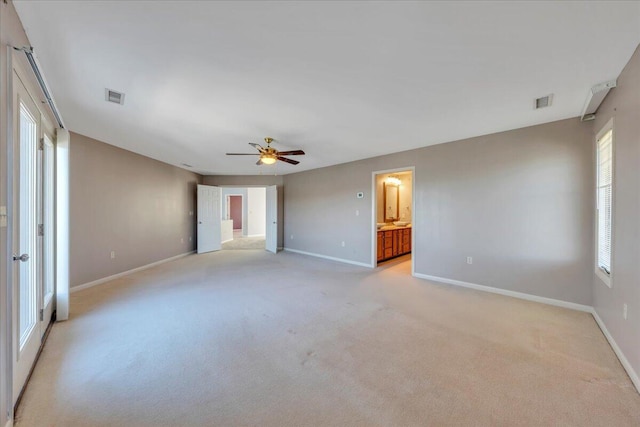 unfurnished bedroom featuring baseboards, visible vents, ensuite bath, ceiling fan, and light colored carpet