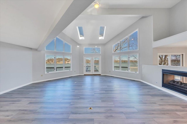 unfurnished living room with a skylight, wood finished floors, and baseboards