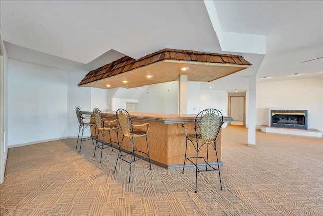 bar featuring a glass covered fireplace, baseboards, and light carpet