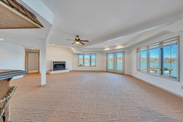 unfurnished living room featuring a glass covered fireplace, baseboards, light carpet, and ceiling fan