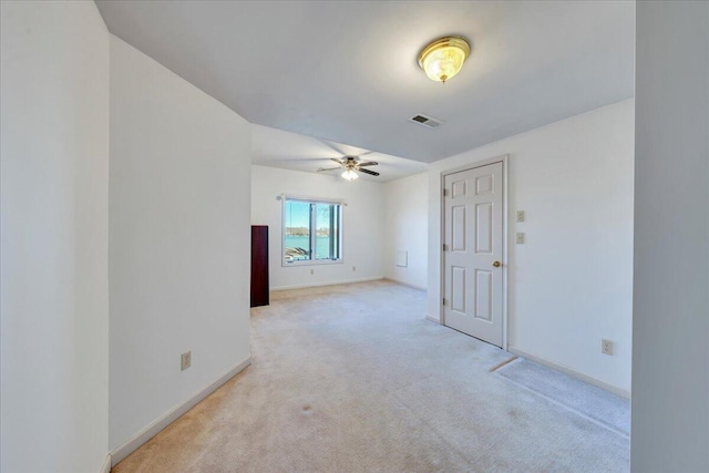 carpeted spare room with visible vents, baseboards, and ceiling fan