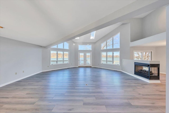 unfurnished living room featuring wood finished floors, a skylight, baseboards, and a multi sided fireplace