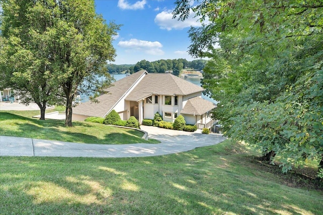 tudor house featuring concrete driveway, a front yard, roof with shingles, stucco siding, and an attached garage