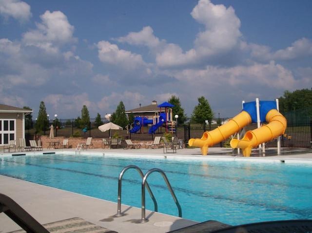 community pool with fence, a water slide, a patio, and playground community