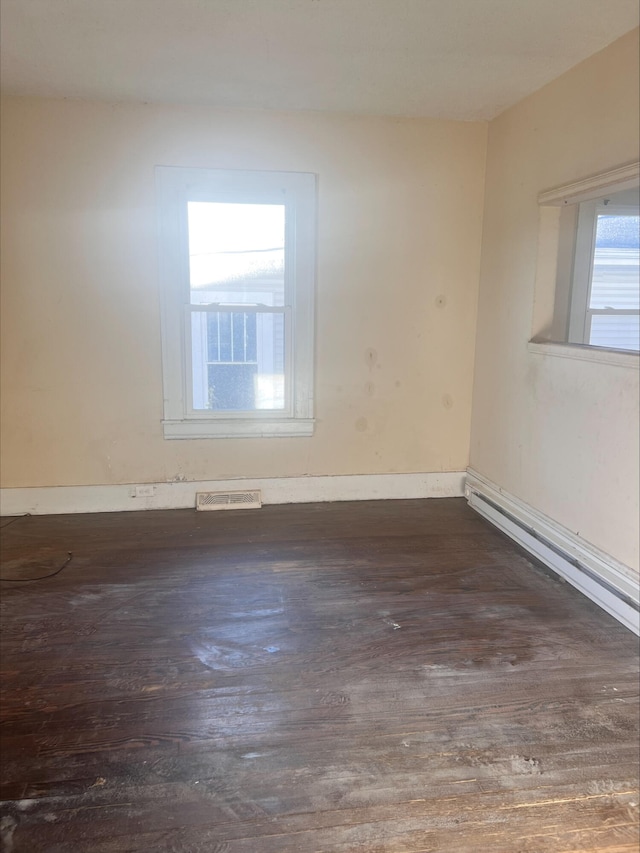 empty room with visible vents, baseboard heating, and wood finished floors