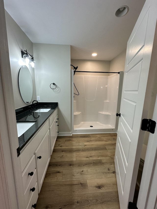 full bathroom featuring double vanity, recessed lighting, a shower, a sink, and wood finished floors