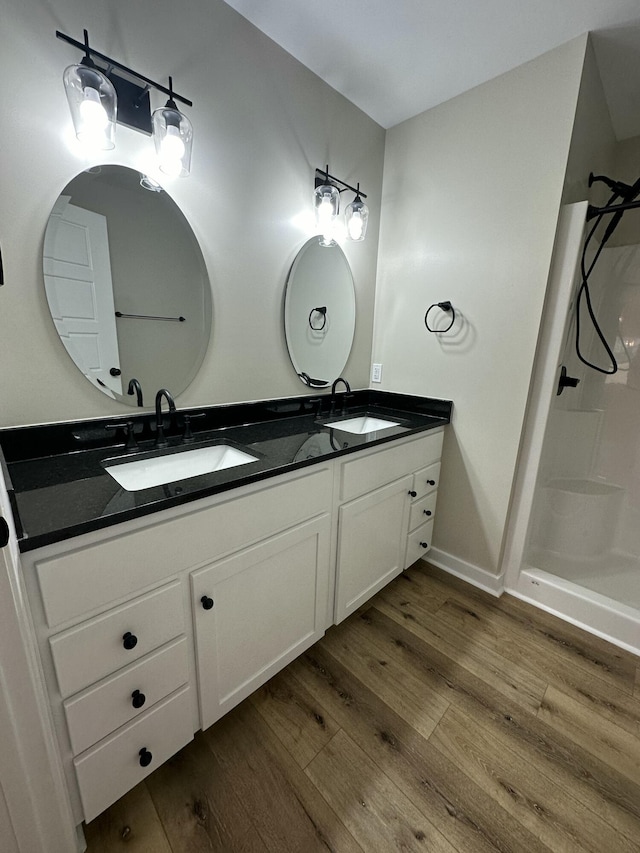 bathroom featuring wood finished floors, double vanity, a sink, and walk in shower