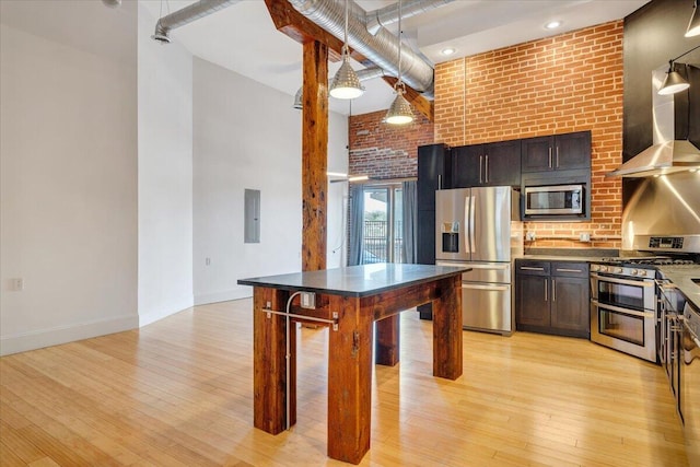 133 Norfolk Ave SW, Roanoke, VA 24011 - kitchen featuring stainless steel appliances, wall chimney range hood, a towering ceiling, light wood-style floors, and brick wall