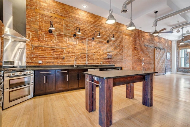 133 Norfolk Ave SW, Roanoke, VA 24011 - kitchen featuring range with two ovens, a barn door, wall chimney exhaust hood, dark countertops, and brick wall