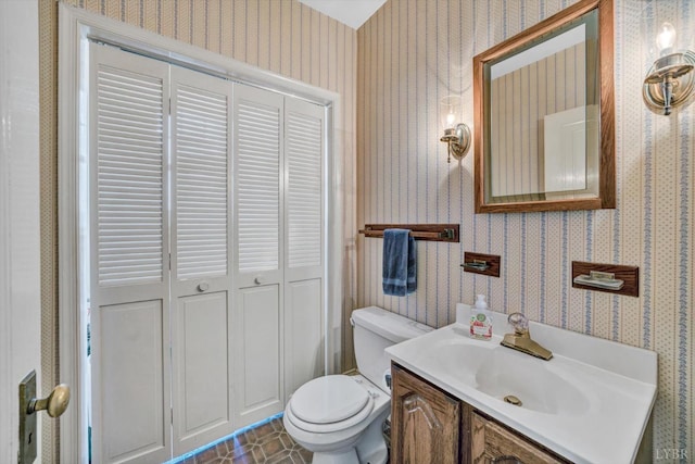half bathroom featuring wallpapered walls, toilet, and vanity