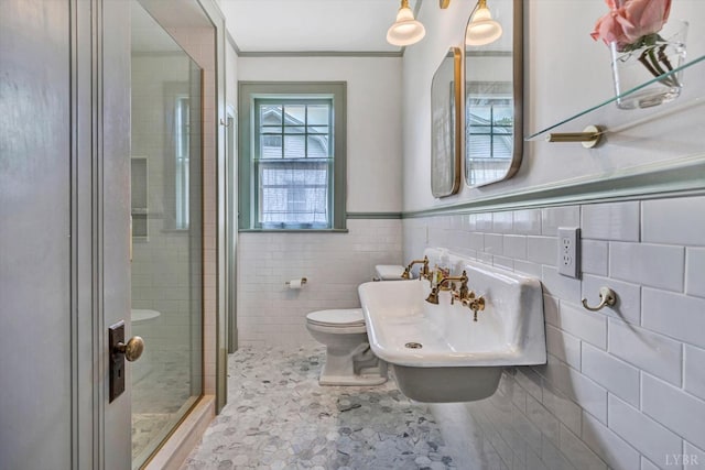 bathroom featuring tile walls, toilet, a wainscoted wall, a sink, and a stall shower
