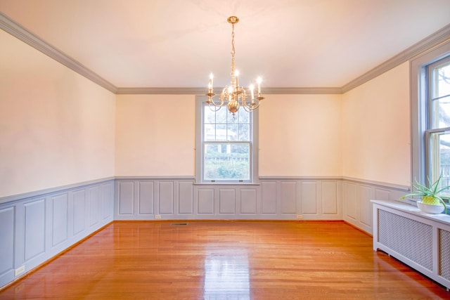 empty room with a healthy amount of sunlight, light wood-type flooring, radiator heating unit, and a chandelier
