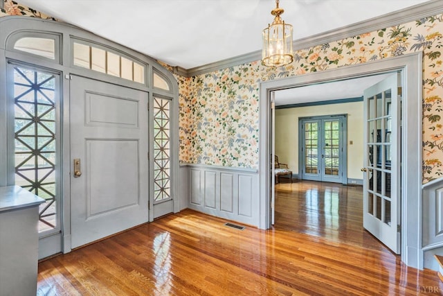 foyer entrance featuring a wainscoted wall, hardwood / wood-style flooring, ornamental molding, wallpapered walls, and french doors