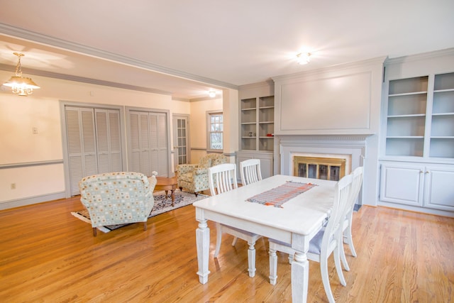 dining space with crown molding, light wood-style flooring, and a glass covered fireplace
