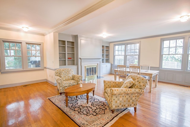 living room featuring built in shelves, a fireplace with flush hearth, visible vents, light wood-style floors, and ornamental molding