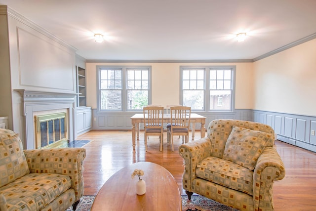 living room featuring built in features, crown molding, light wood finished floors, and wainscoting
