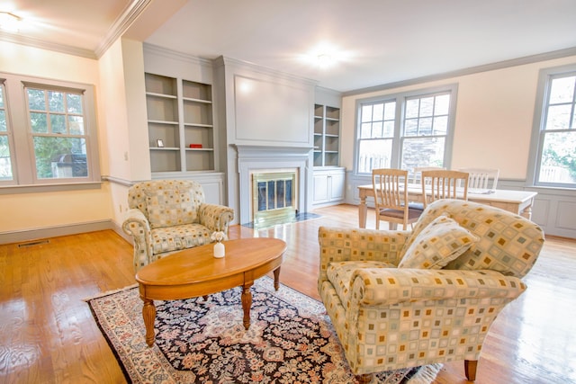 living room with crown molding, a fireplace with flush hearth, built in shelves, light wood finished floors, and visible vents